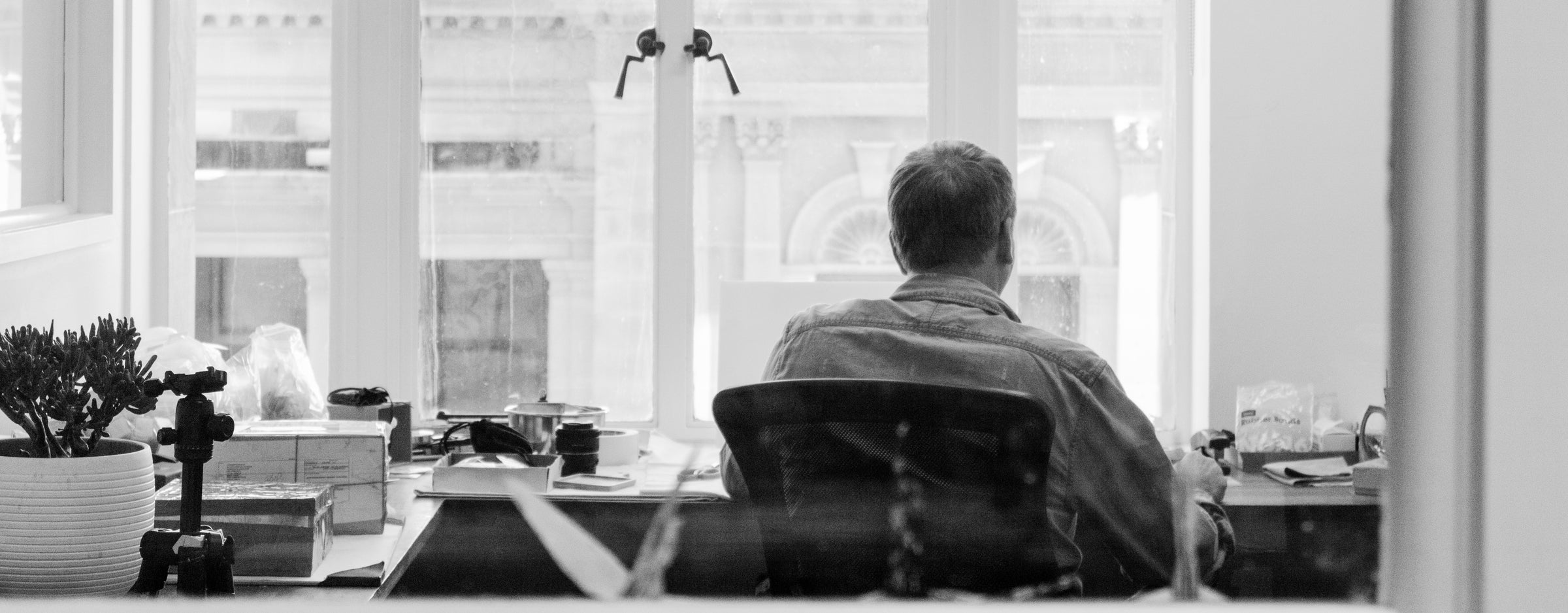 A black and white image of owner and founder, Brendon Maddock sitting at his desk overlooking the  heritage listed Treasury Casino building while sorting through gemstones.