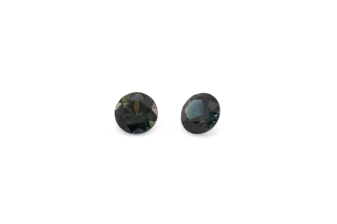 A pair of round brilliant cut blue/green Australian sapphire gemstones are displayed on a white background.