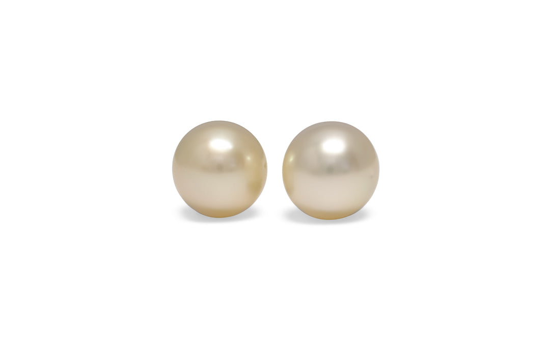A pair of semi round, cream, white south sea pearls are displayed on a white background.