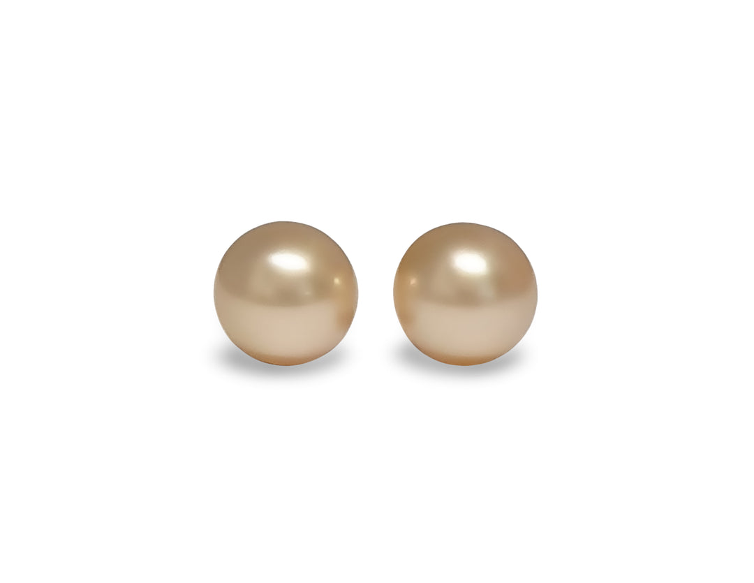 A pair of semi round, pink gold, golden south sea pearls are displayed on a white background.