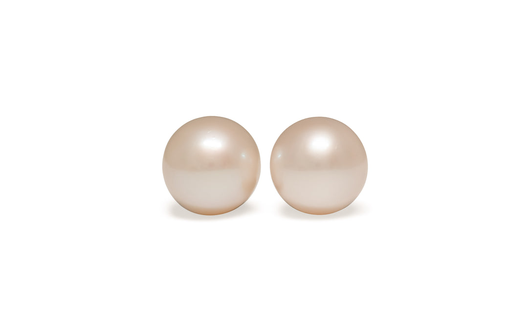 A pair of semi round, pink, white south sea pearls are displayed on a white background.