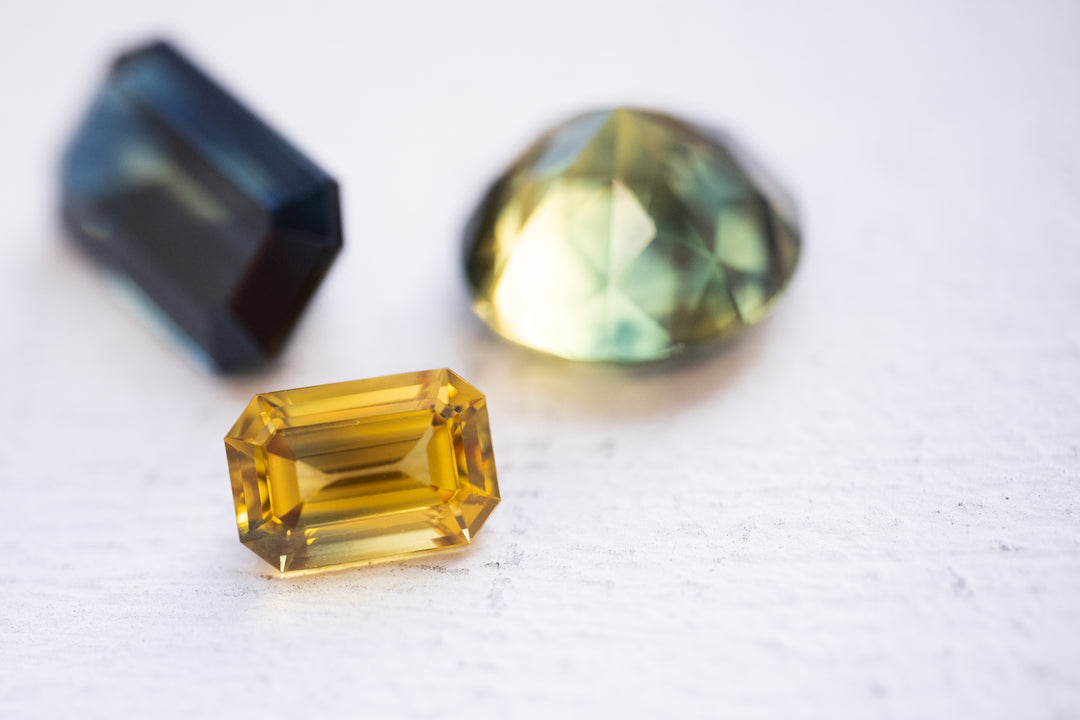 A rare golden yellow Australian sapphire is the star of this image with a couple of parti sapphires out of focus in the background.
