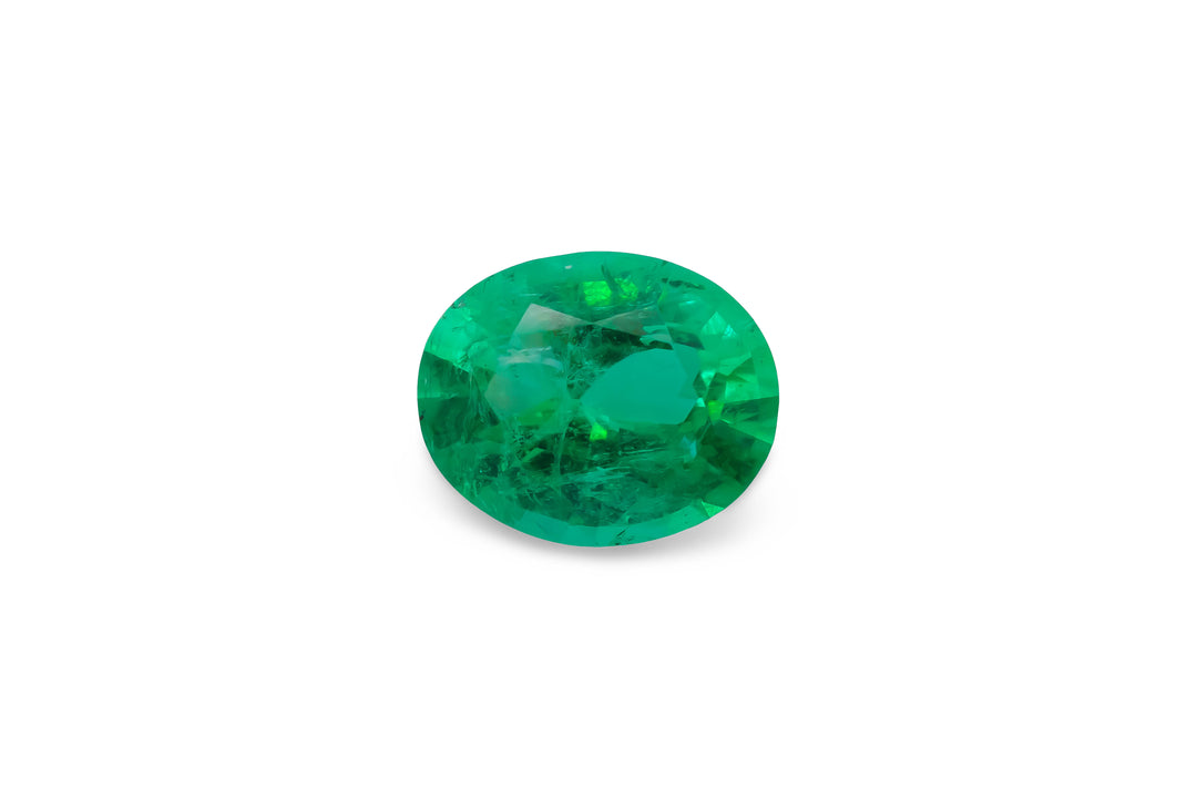 An oval cut Colombian emerald gemstone is displayed on a white background.