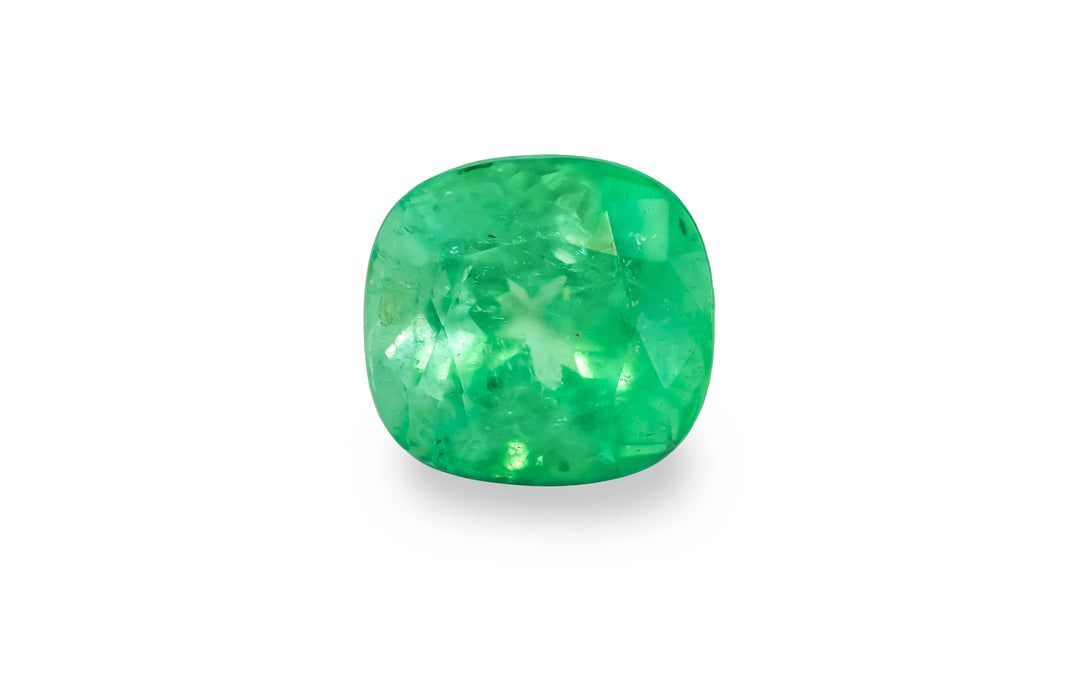 A cushion cut green Colombian emerald gemstone is displayed on a white background.