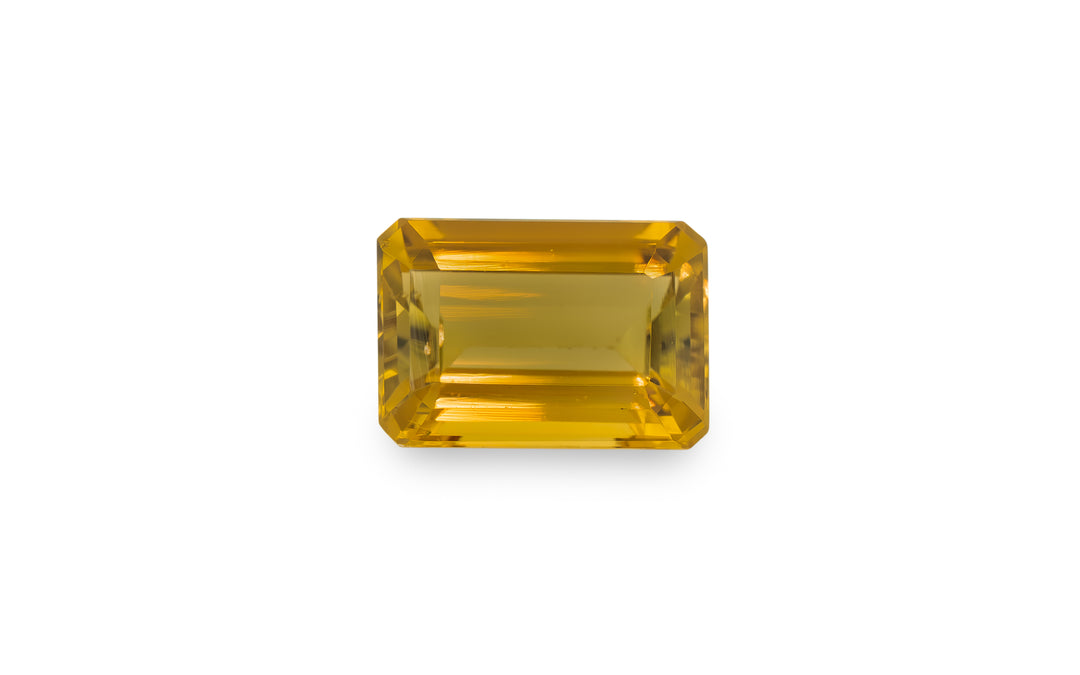 An emerald cut golden yellow tourmaline gemstone is displayed on a white background.