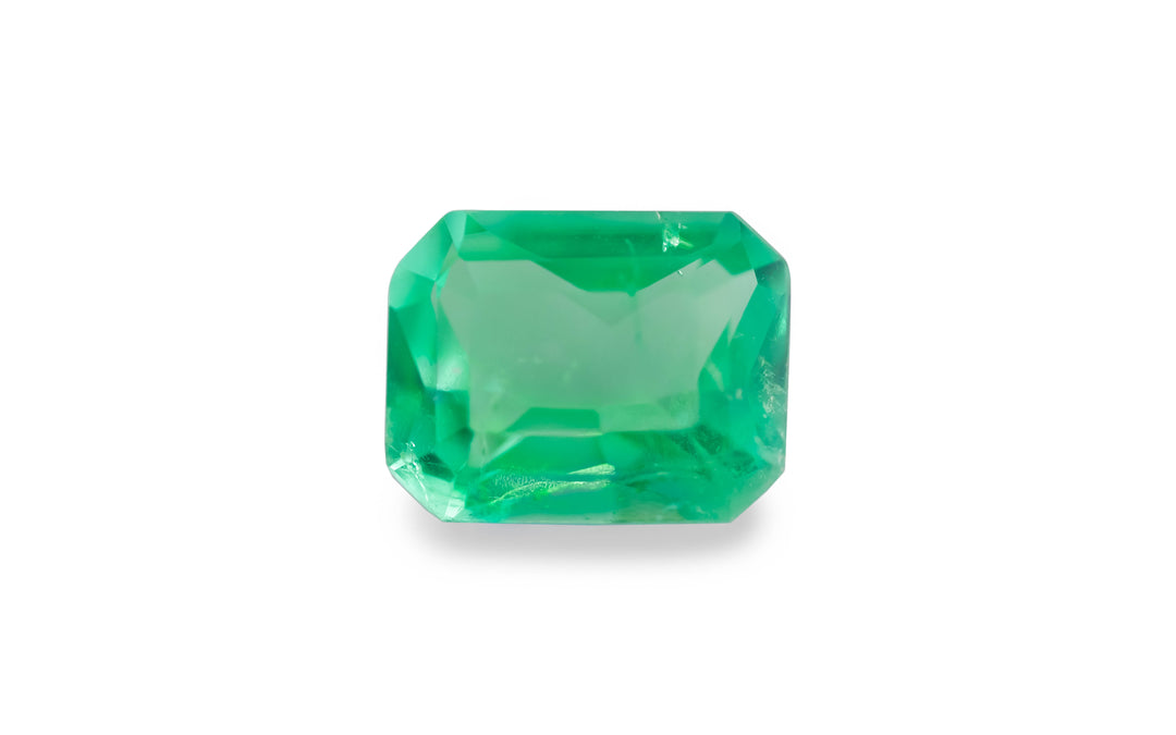 An emerald cut green Colombian emerald gemstone is displayed on a white background.