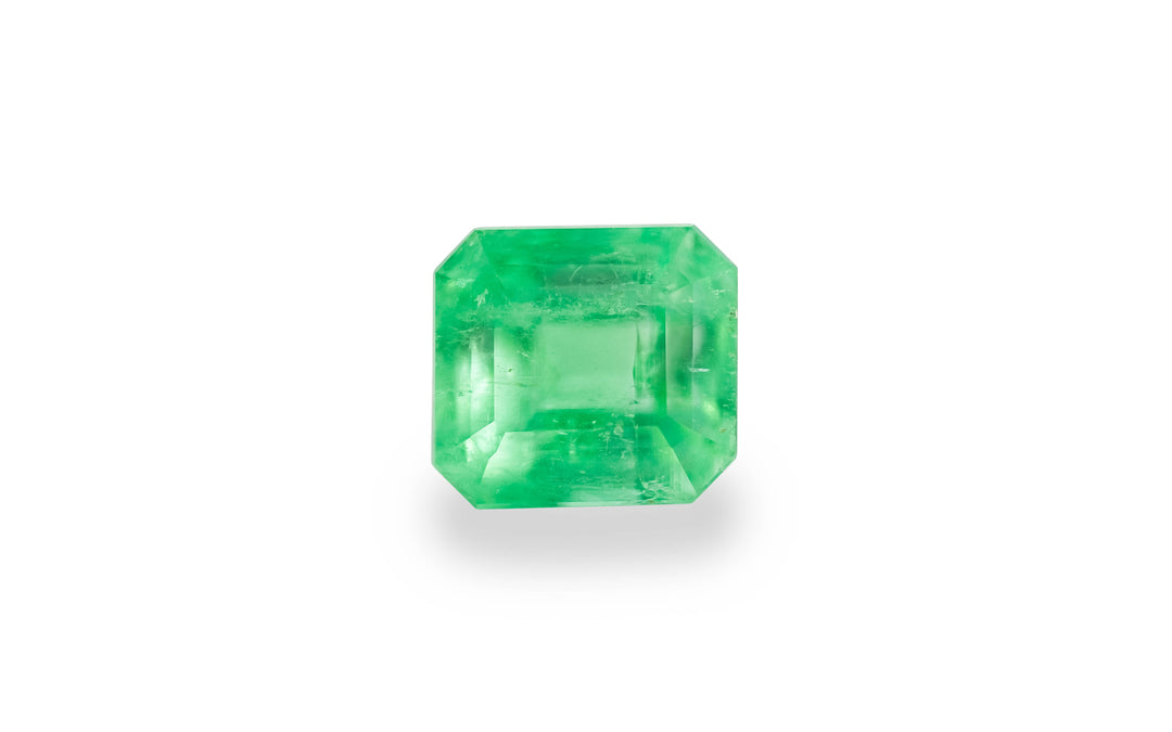 An emerald cut green Colombian emerald gemstone is displayed on a white background.
