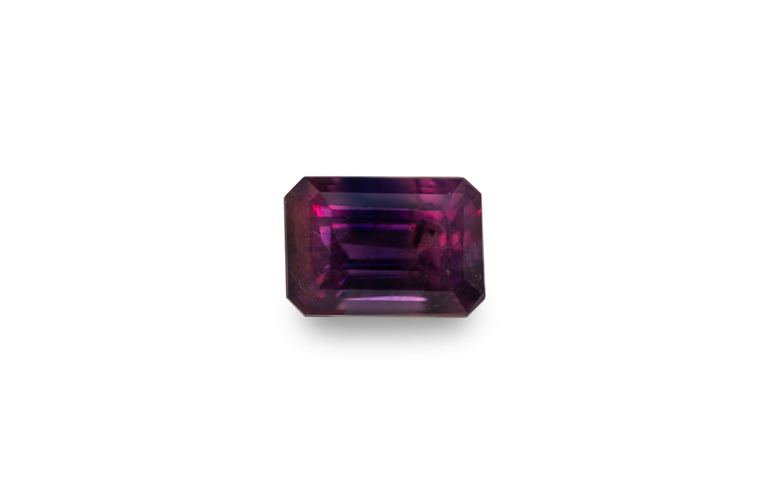 An emerald cut vibrant pink and deep blue Winza sapphire gemstone is displayed on a white background.
