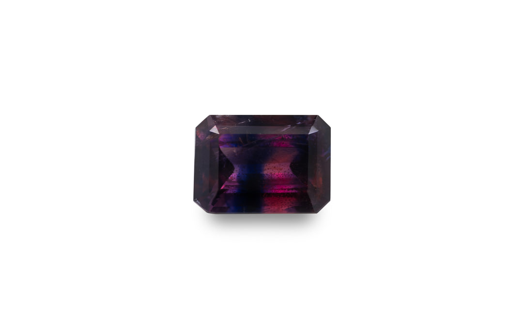 An emerald cut vibrant pink and deep purple blue Winza sapphire gemstone is displayed on a white background.