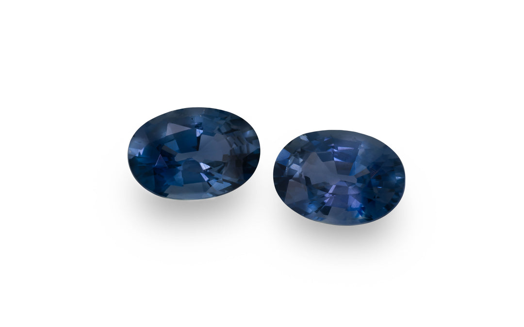 A pair of blue oval cut Australian sapphire gemstones is displayed on a white background.