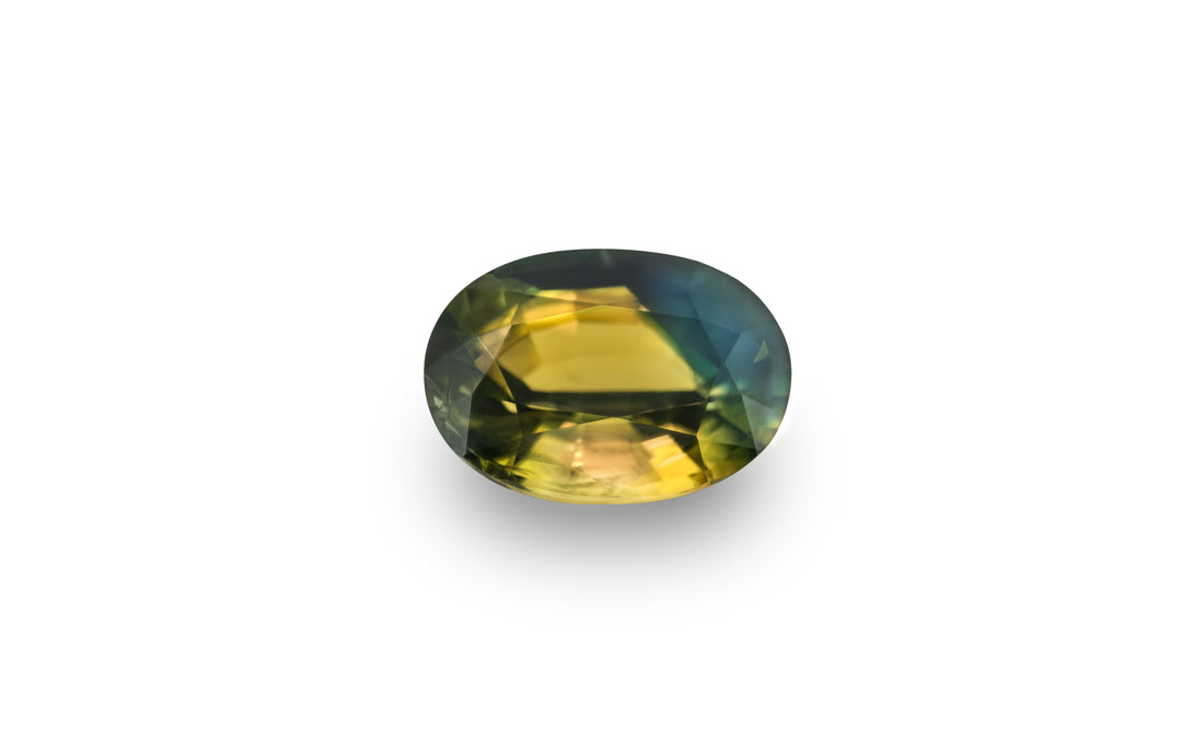 An oval cut, bright yellow, deep blue and green Australian parti sapphire gemstone is displayed on a white background.