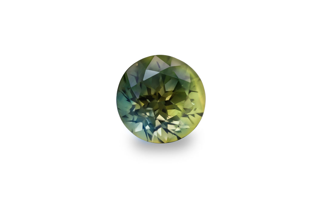 A round cut, bright green/yellow and deep blue Australian Parti sapphire gemstone is displayed on a white background.