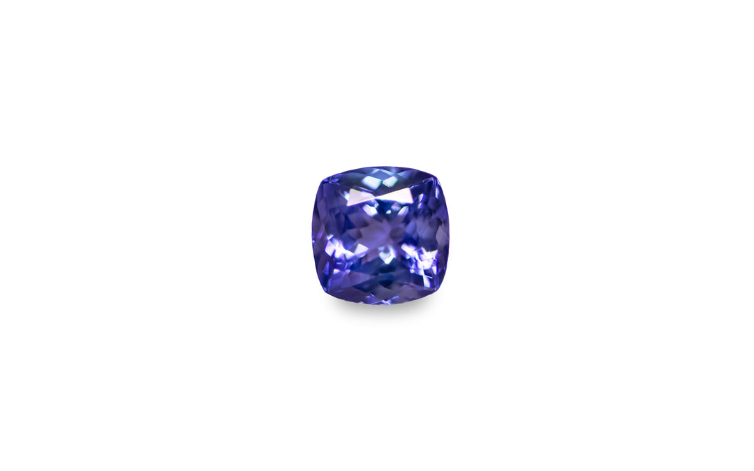 A cushion cut purple blue Tanzanite gemstone is displayed on a white background.
