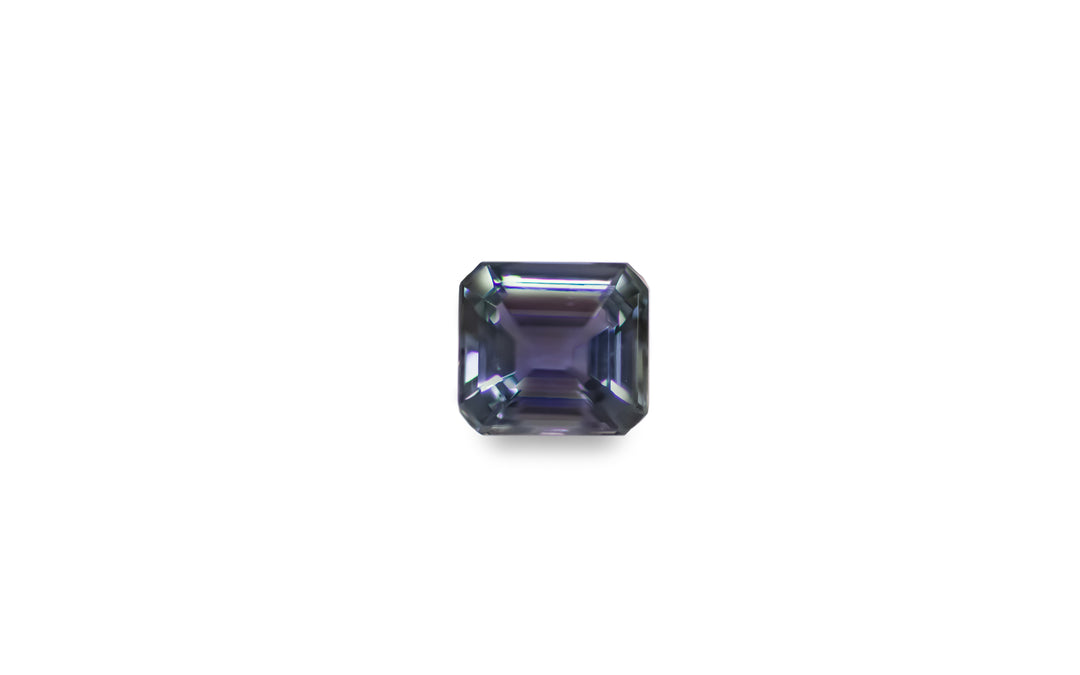 An emerald cut purple blue green Tanzanite is displayed on a white background.