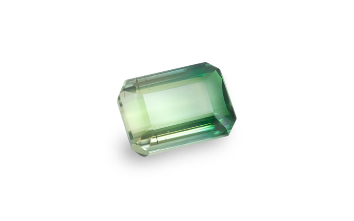 An emerald cut bi colour green tourmaline gemstone is displayed on a white background.
