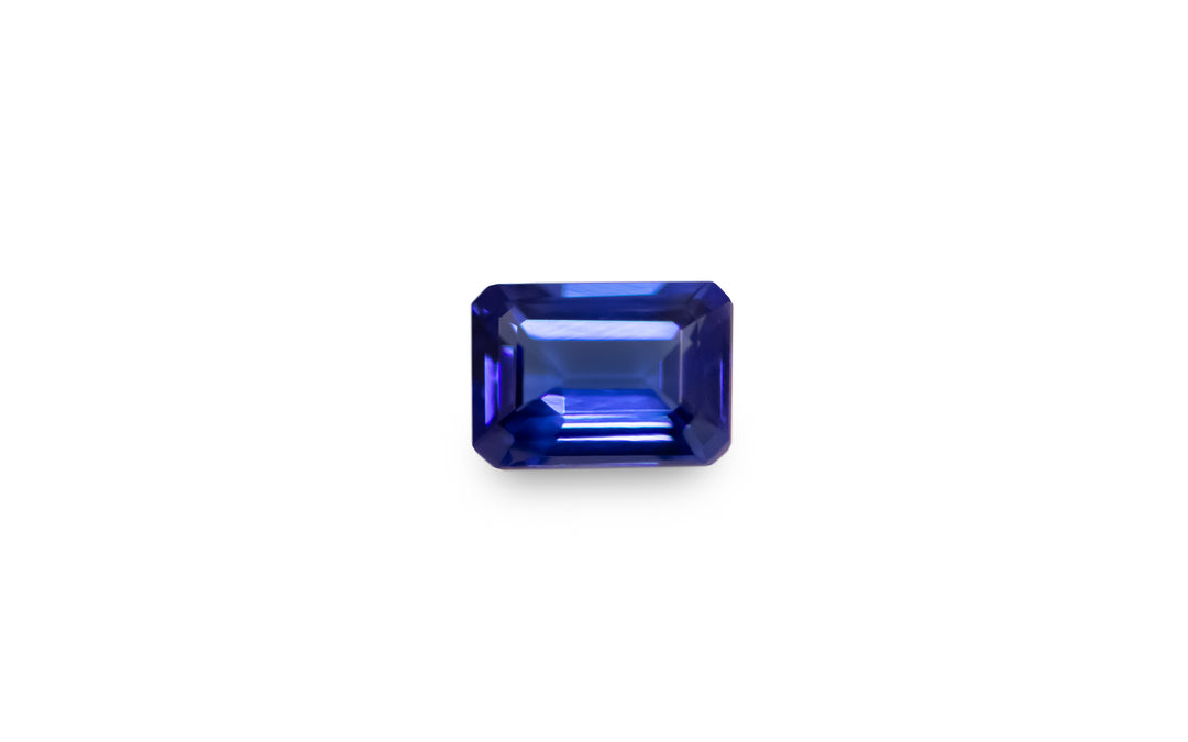 An emerald cut intense blue Tanzanite is displayed on a white background.
