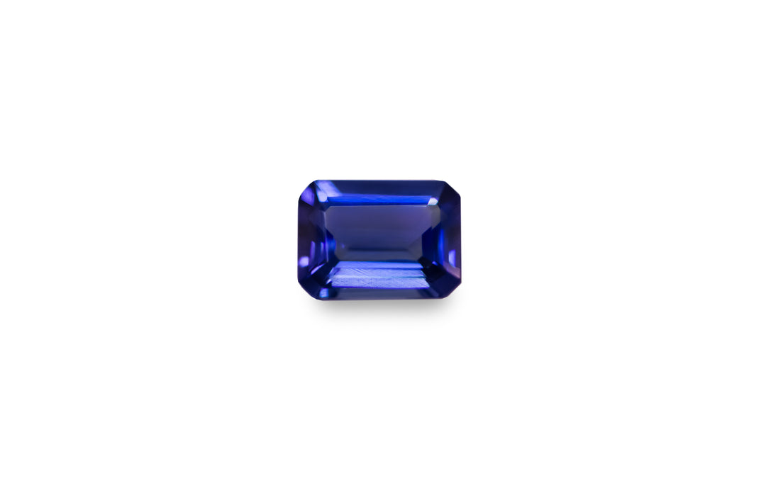An emerald cut purple blue Tanzanite gemstone is displayed on a white background. 