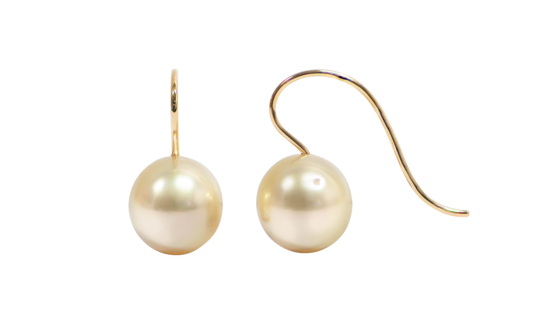 A pair of 18K yellow gold oval pink golden south sea pearl shepherd hook earrings is displayed on a white background.