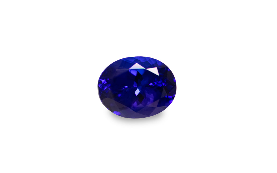 An oval cut intense blue Tanzanite gemstone is displayed on a white background.