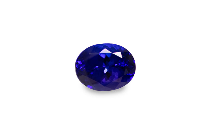 An oval cut intense blue Tanzanite gemstone is displayed on a white background.