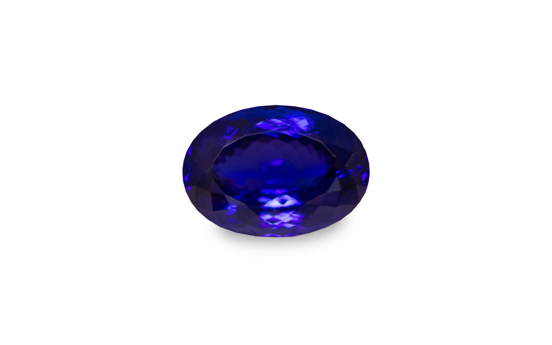 An oval cut intense blue Tanzanite gemstone is displayed on a white background.