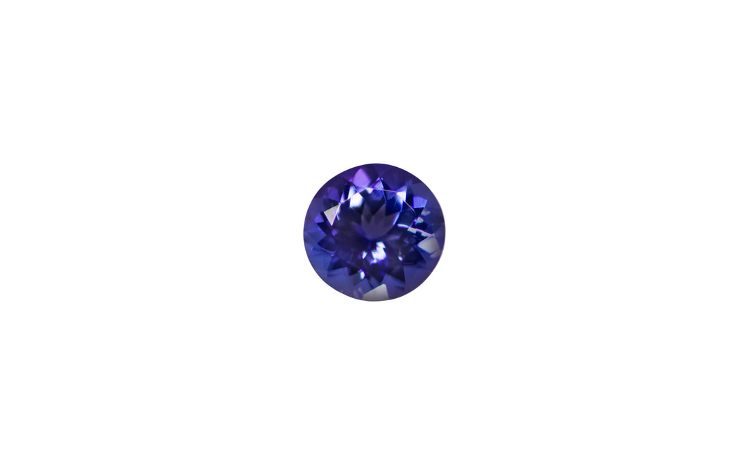 A round cut intense purple blue Tanzanite gemstone is displayed on a white background.