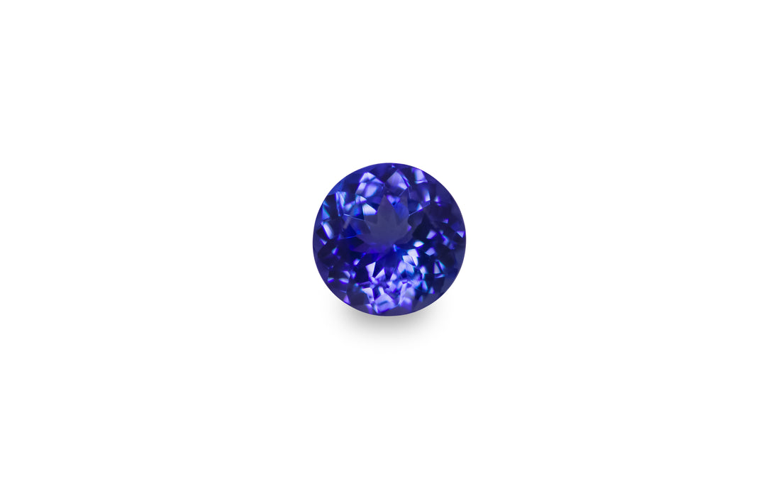 A round cut purple blue Tanzanite gemstone is displayed on a white background. 