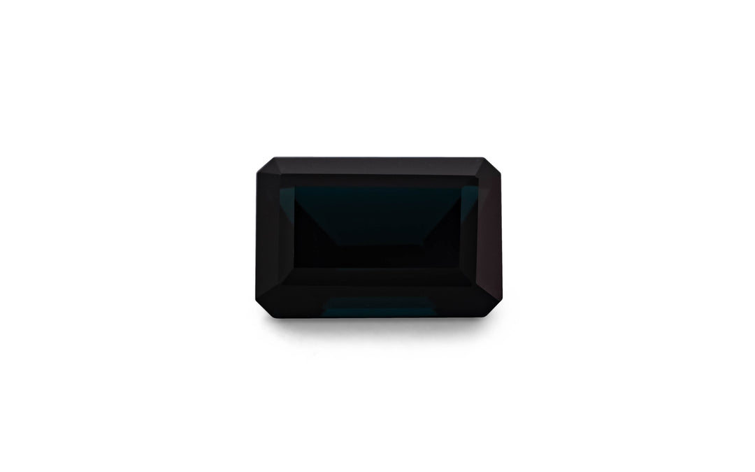 An emerald cut black blue spinel gemstone is displayed on a white background.