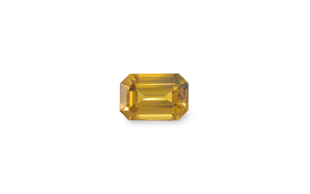 An emerald cut golden yellow Australian sapphire gemstone is displayed on a white background.
