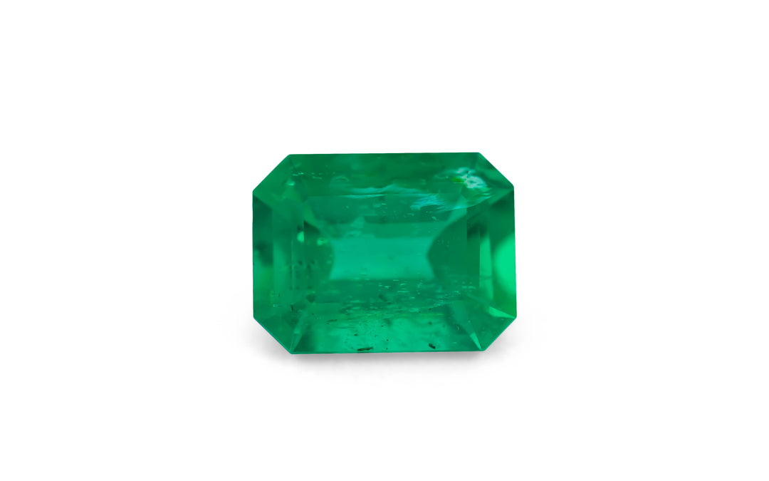 An emerald cut green Zambian emerald gemstone is displayed on a white background.