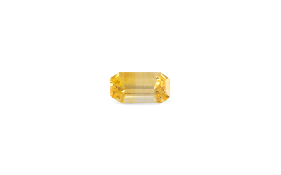 An emerald cut golden yellow Ceylon sapphire gemstone is displayed on a white background.
