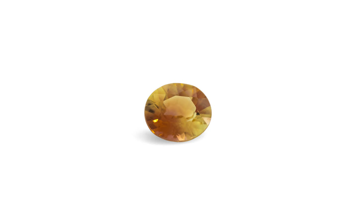 An oval cut, bi-colour yellow and orange tourmaline gemstone is displayed on a white background.