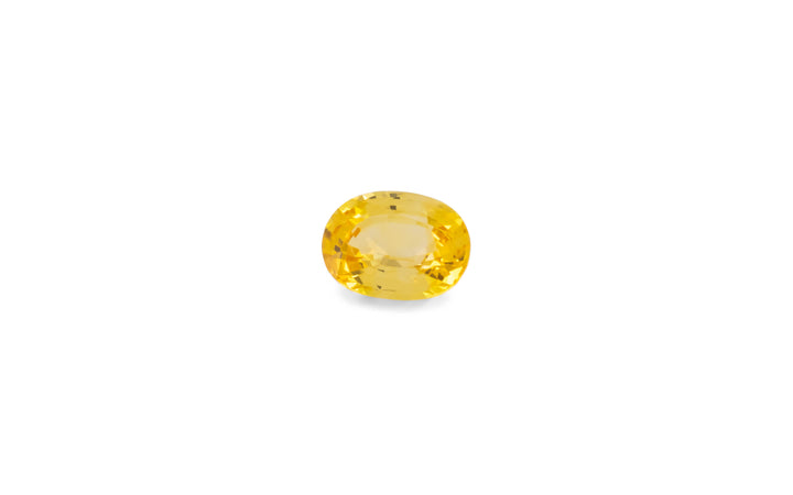 An oval cut golden yellow Ceylon sapphire gemstone is displayed on a white background.