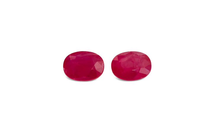 A pair of oval cut, red Burmese ruby gemstones are displayed on a white background.