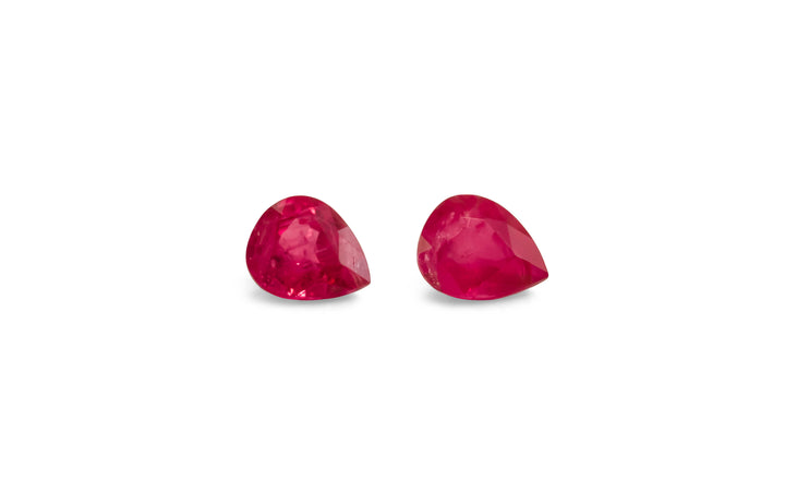 A pair of pear cut, red Burmese ruby gemstones are displayed on a white background.