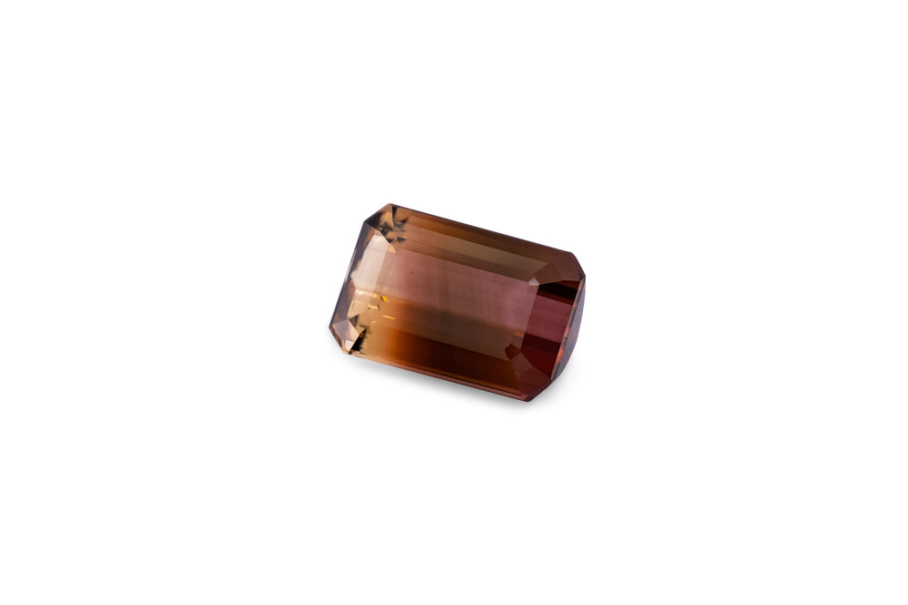 An emerald cut deep pink and yellow  bi-colour tourmaline gemstone is displayed on a white background.