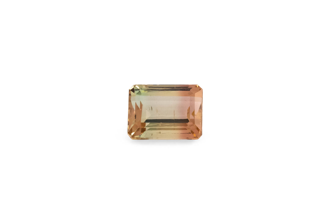 An emerald cut bi-colour pink and yellow tourmaline gemstone is displayed on a white background.
