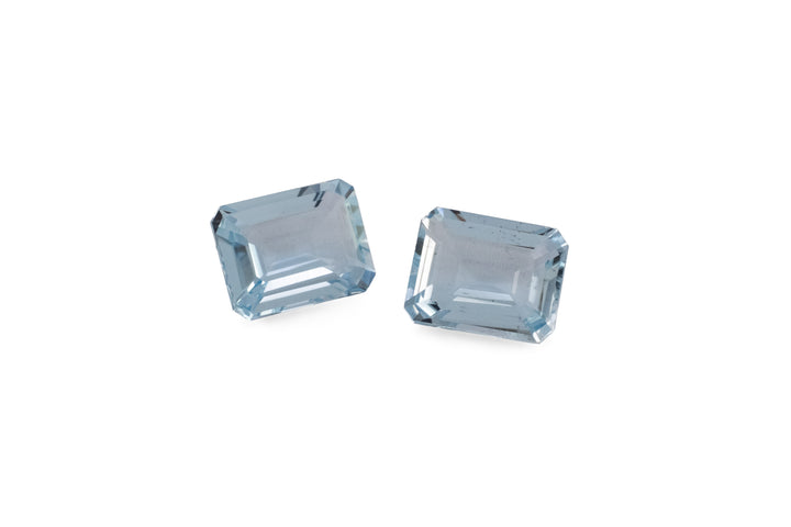 A pair of emerald cut pale blue aquamarine gemstones are displayed on a white background.