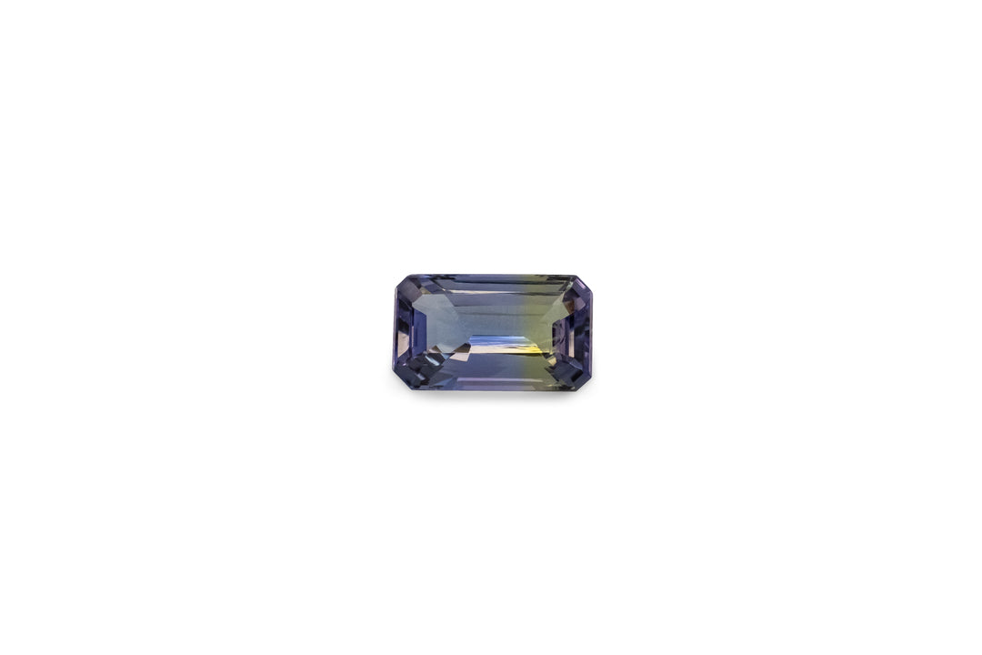 An emerald cut untreated bi-colour blue and yellow tanzanite gemstone is displayed on a white background.