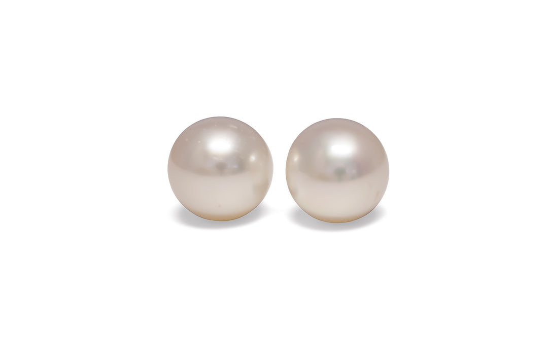 A pair of high button, pink, white south sea pearls are displayed on a white background.