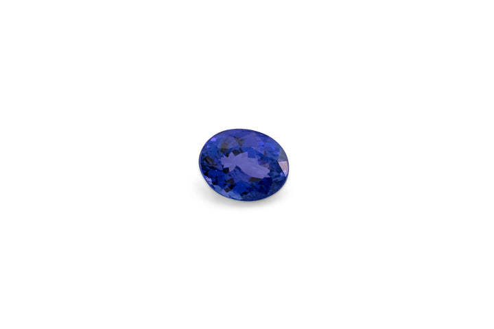An oval cut intense blue Tanzanite gemstone is displayed on a white background.
