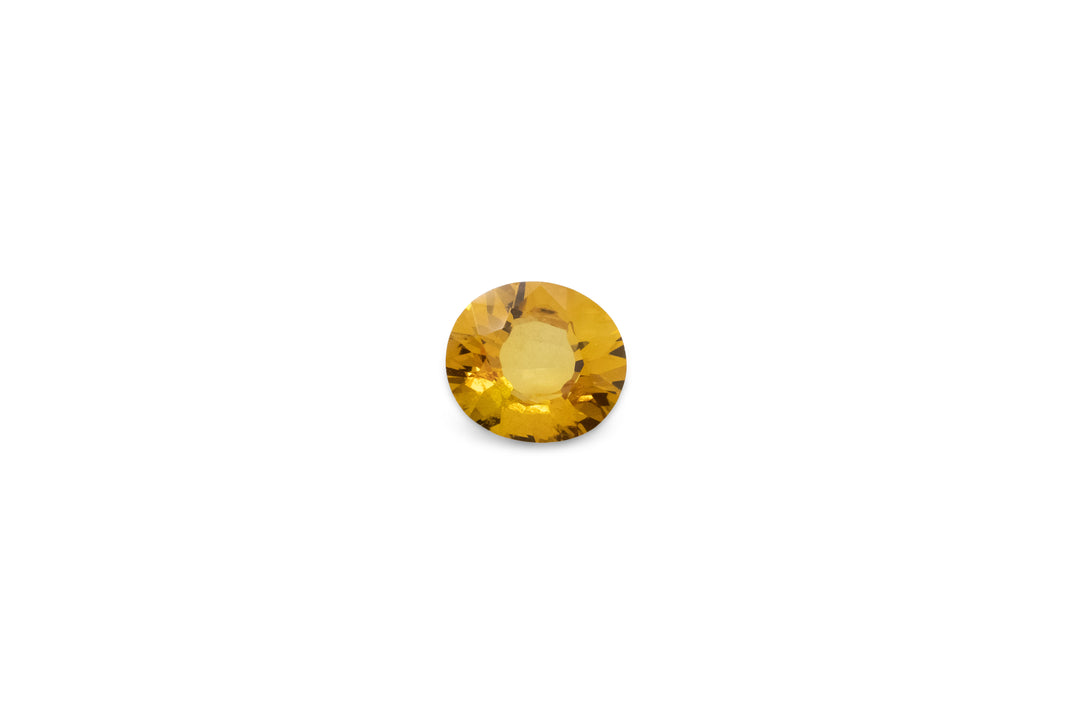 A oval cut golden yellow Ceylon sapphire gemstone is displayed on a white background.