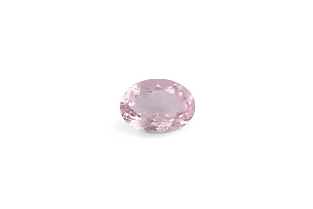 An oval cut pale pink morganite gemstone is displayed on a white background.