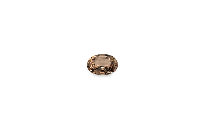 An oval cut, umber brown Ceylon sapphire is displayed on a white background.