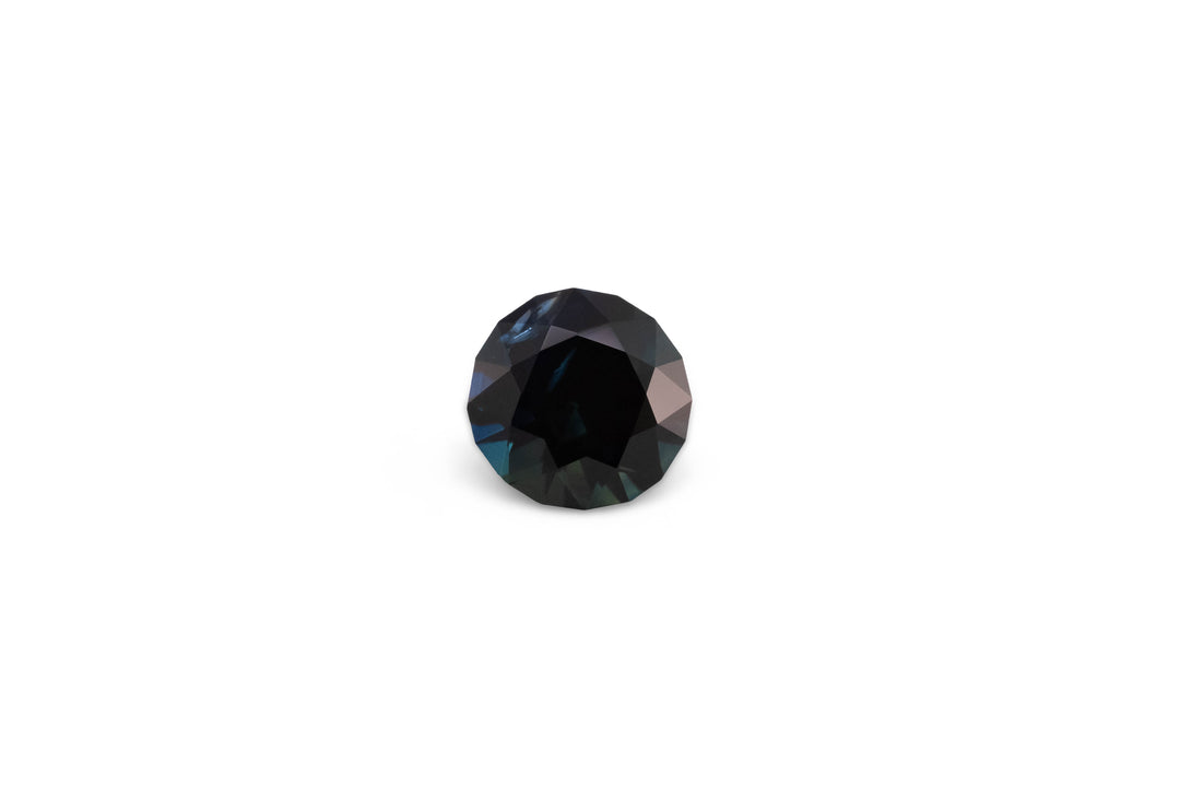 A round brilliant cut deep blue Australian sapphire gemstone is displayed on a white background.