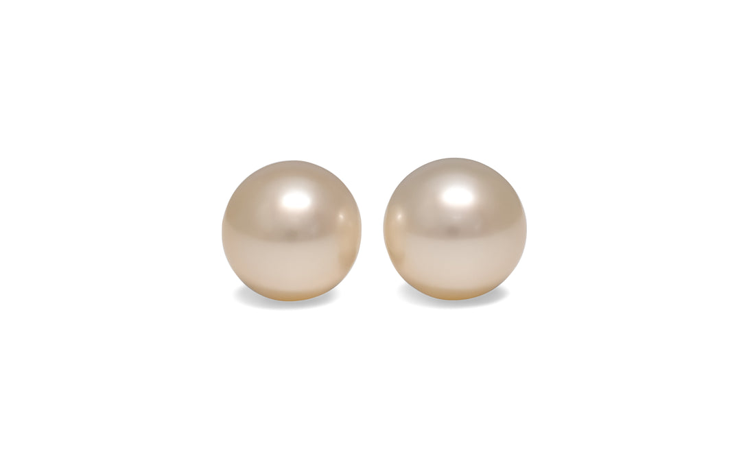 A pair of round, cream, white south sea pearls are displayed on a white background.