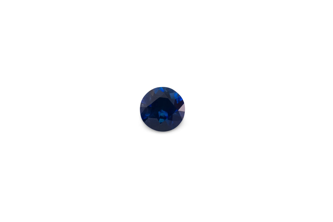 A round cut vivid blue Ceylon sapphire gemstone is displayed on a white background.