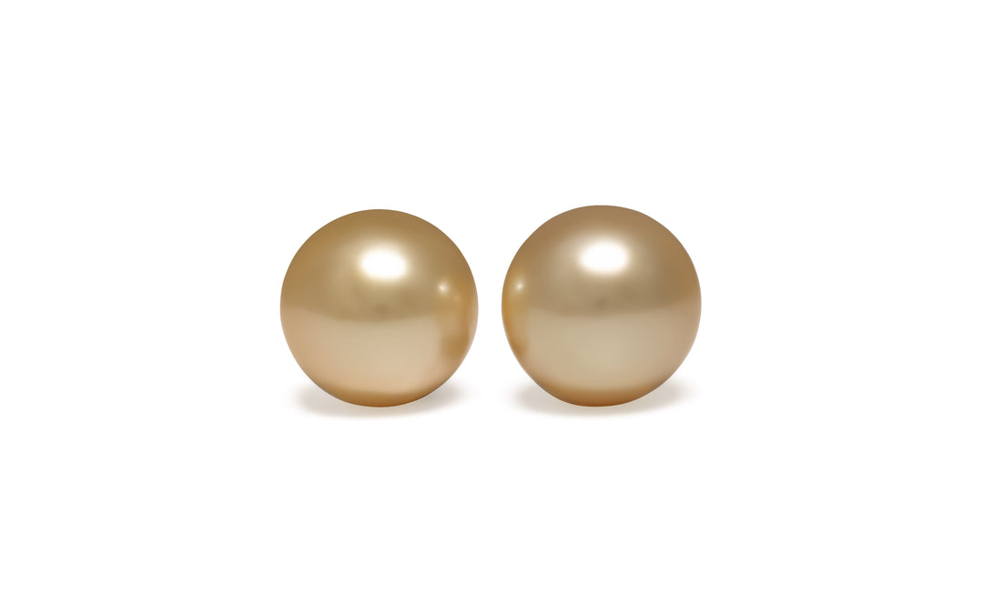 A pair of round golden South Sea Pearls is displayed on a white background.