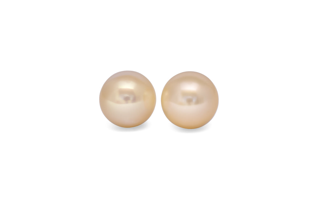 A pair of round, cream, white south sea pearls are displayed on a white background.