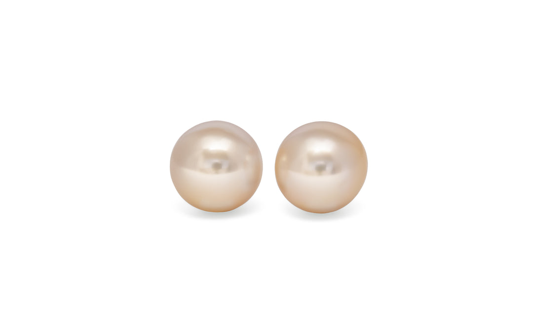 A pair of semi round golden south sea pearls are displayed on a white background.